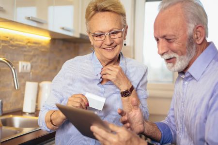 An elderly couple shopping online with an iPad and credit card in their hands