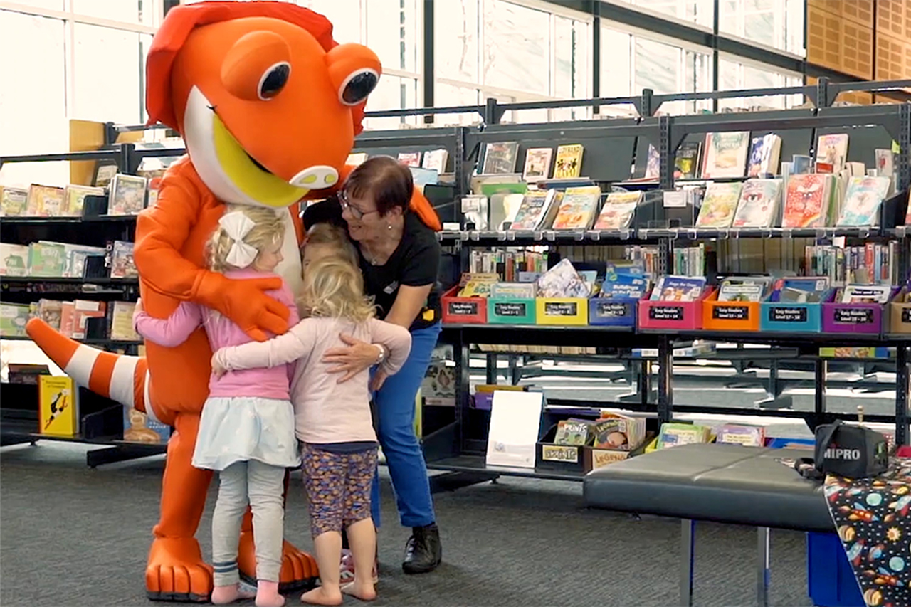 Lizzie the Literacy Lizard hugging librarian and kids