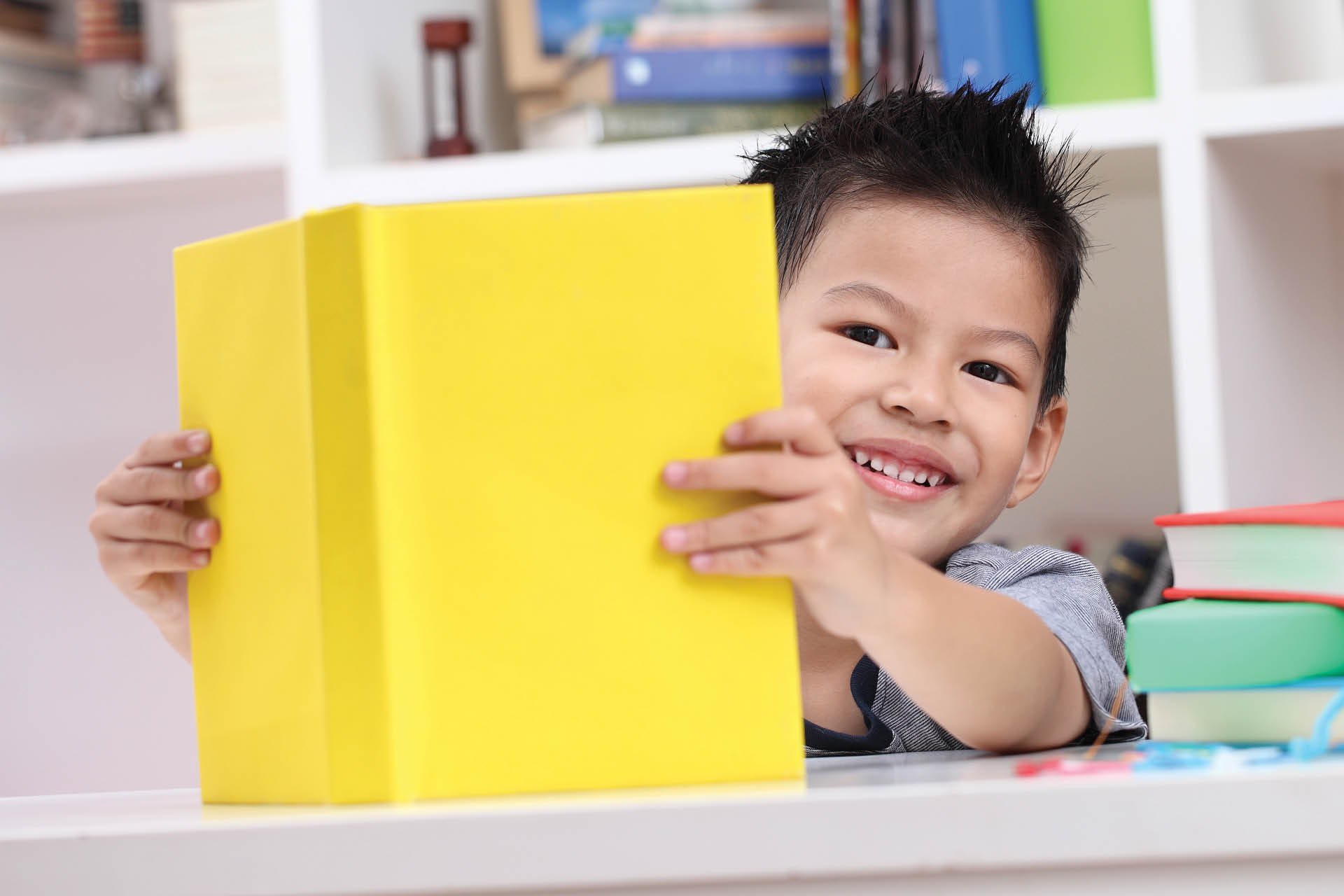 Young kid holding up yellow book and smiling